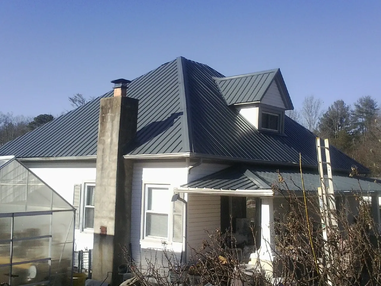 Dark blue standing seam metal roof on a white farmhouse with dormer — Slate & Tile Roof Repair by Roofing Brothers in Sunset