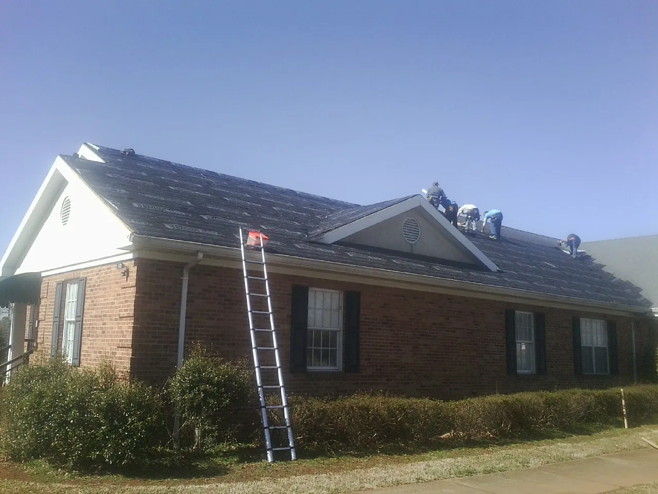 Crew tearing shingles off a brick ranch roof with a ladder set — Metal Roof Repair work by our crew in Sunset