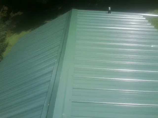 New green metal panels meeting at the ridge of a roof — Flat Roof Repair work by our crew in Sunset